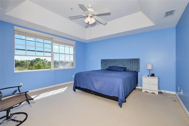 carpeted bedroom with ceiling fan and a raised ceiling