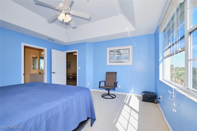 carpeted bedroom with ceiling fan, ensuite bath, and a tray ceiling