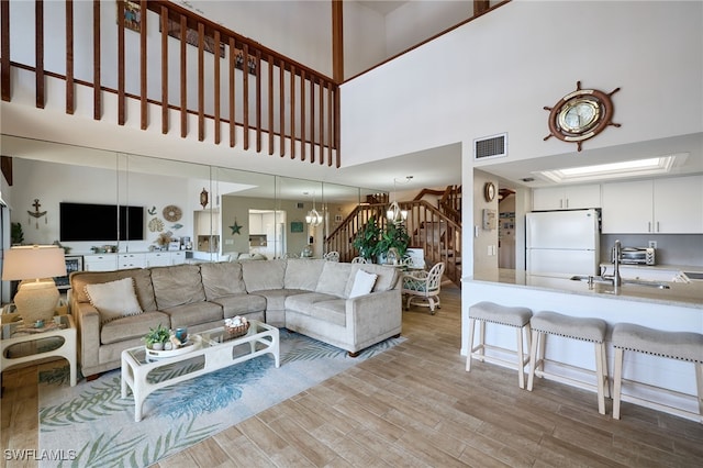 living room with sink, light wood-type flooring, and a high ceiling