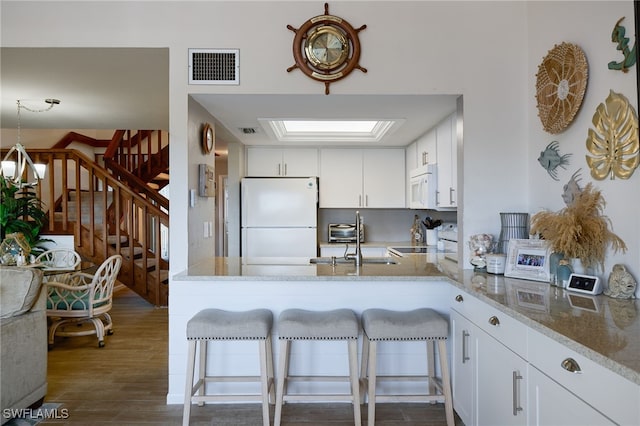 kitchen featuring a breakfast bar, white cabinetry, kitchen peninsula, white appliances, and light stone countertops