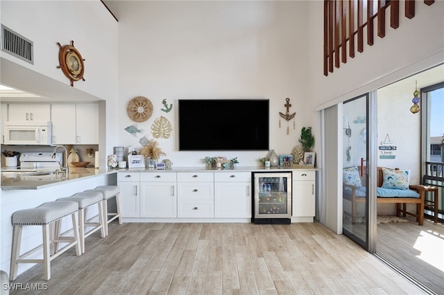 kitchen featuring white appliances, white cabinetry, a high ceiling, beverage cooler, and light wood-type flooring