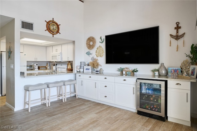 kitchen with white cabinetry, wine cooler, white appliances, and light hardwood / wood-style floors