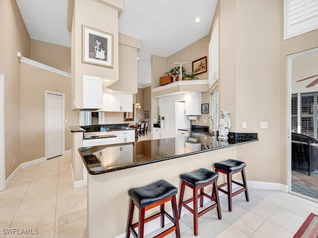 kitchen with light tile patterned floors, kitchen peninsula, sink, and white cabinets