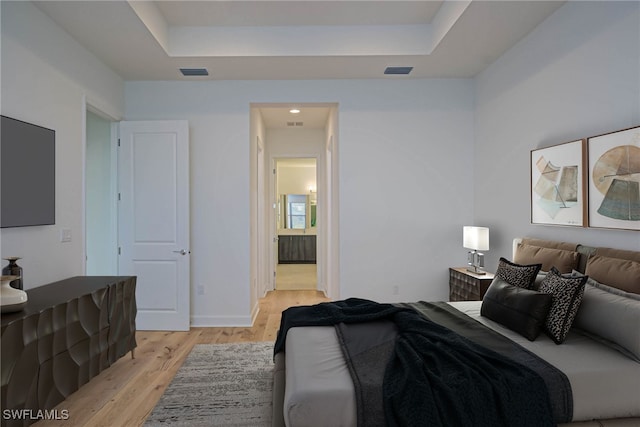 bedroom featuring connected bathroom, a tray ceiling, and light wood-type flooring