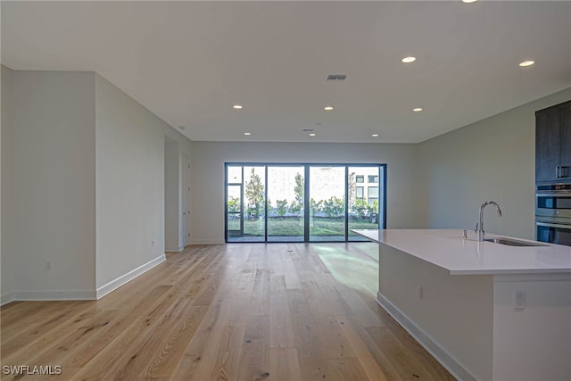 kitchen featuring double oven, sink, light hardwood / wood-style flooring, and a center island with sink