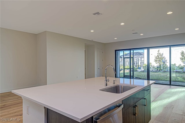 kitchen with dishwasher, an island with sink, sink, dark brown cabinets, and light wood-type flooring