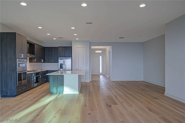 kitchen featuring appliances with stainless steel finishes, dark brown cabinets, a center island with sink, and light wood-type flooring