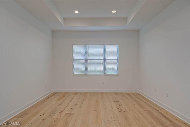 empty room featuring light wood-type flooring and a tray ceiling