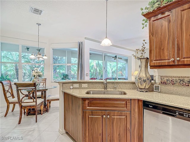 kitchen with decorative light fixtures, dishwasher, sink, light tile patterned floors, and light stone counters