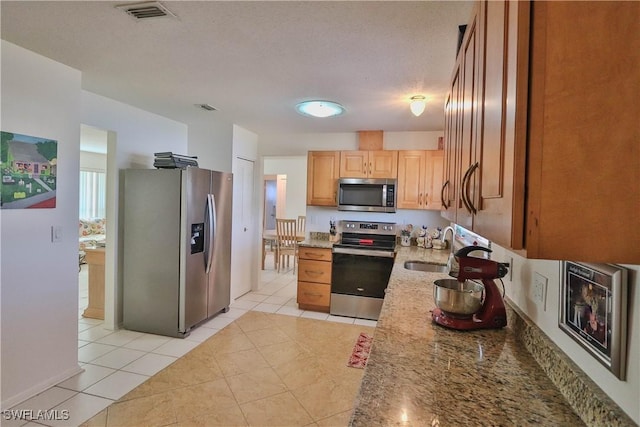 kitchen with sink, a textured ceiling, light tile patterned floors, stainless steel appliances, and light stone countertops