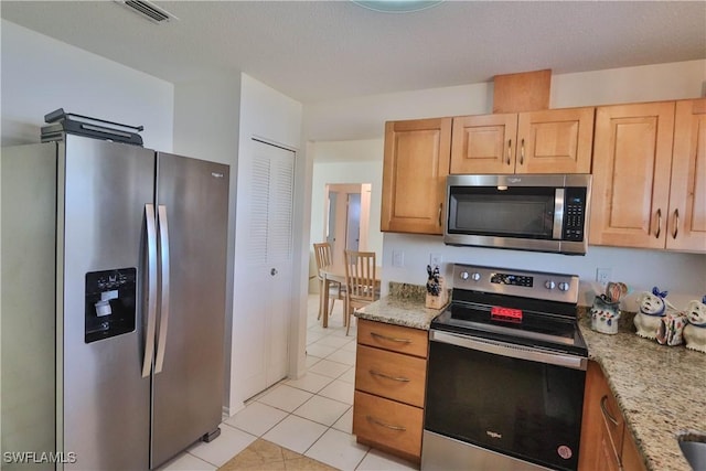 kitchen featuring stainless steel appliances, light tile patterned floors, light stone counters, and light brown cabinets