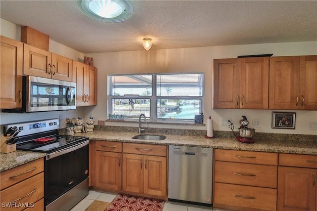 kitchen with sink, a textured ceiling, light tile patterned floors, appliances with stainless steel finishes, and light stone countertops