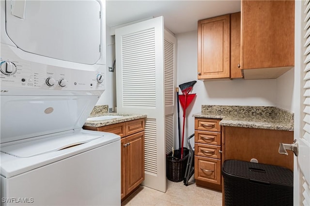 laundry room featuring light tile patterned flooring, cabinets, and stacked washer / dryer