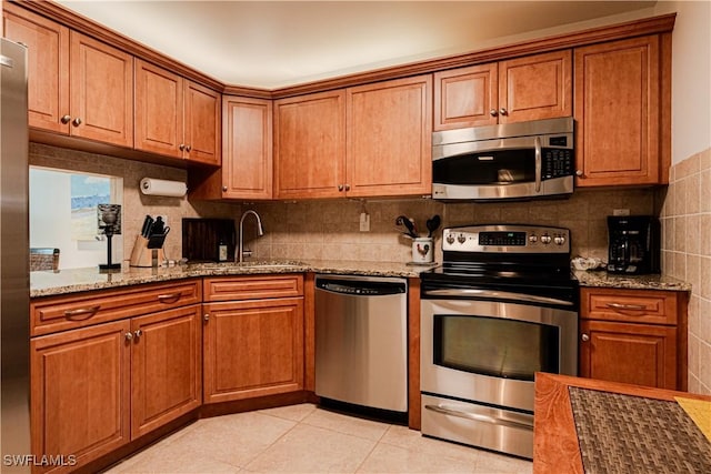 kitchen with sink, light stone counters, tasteful backsplash, light tile patterned floors, and appliances with stainless steel finishes