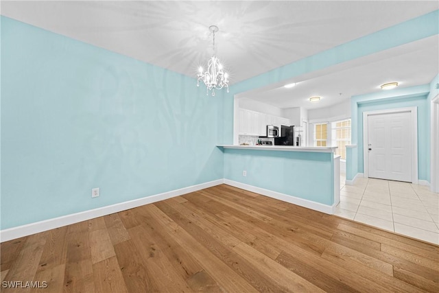 interior space with refrigerator, white cabinets, decorative light fixtures, kitchen peninsula, and light wood-type flooring