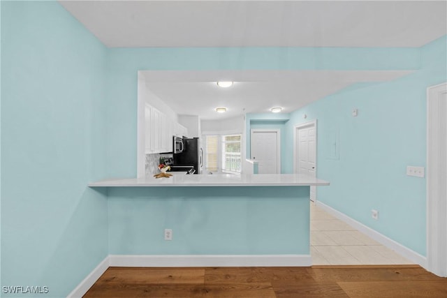 kitchen featuring appliances with stainless steel finishes, white cabinets, decorative backsplash, kitchen peninsula, and light hardwood / wood-style flooring