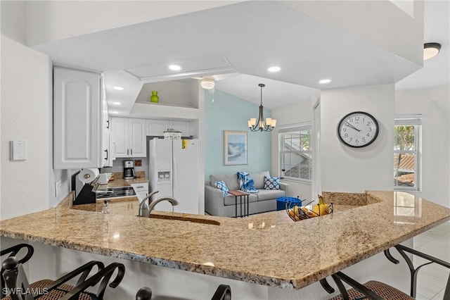 kitchen with lofted ceiling, sink, white cabinetry, kitchen peninsula, and white fridge with ice dispenser