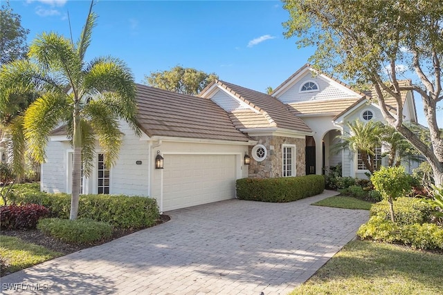 view of front of house with a tiled roof, stone siding, decorative driveway, and an attached garage