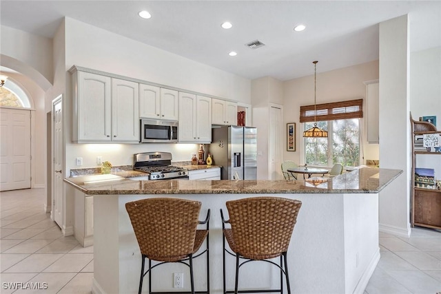 kitchen featuring stone countertops, stainless steel appliances, white cabinetry, a kitchen breakfast bar, and hanging light fixtures