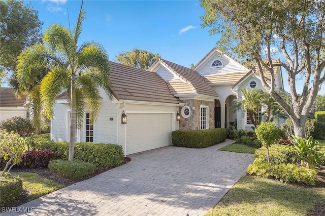 traditional-style home with a tiled roof, decorative driveway, stone siding, and a garage