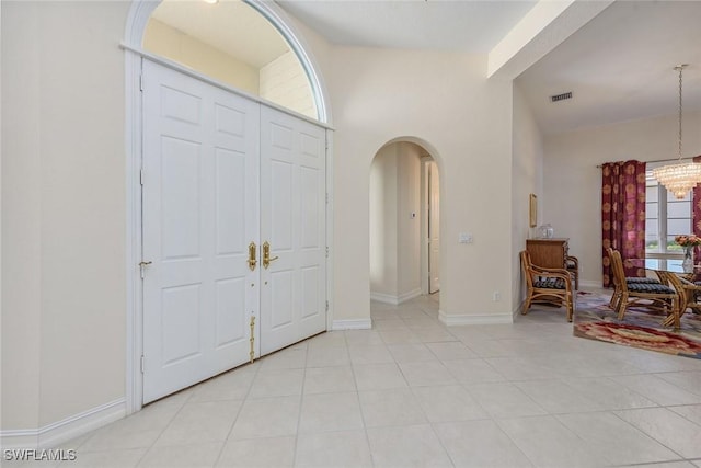 foyer featuring an inviting chandelier, arched walkways, baseboards, light tile patterned floors, and visible vents