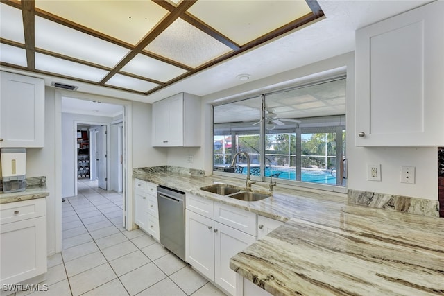 kitchen with light tile patterned floors, light stone counters, a sink, white cabinetry, and stainless steel dishwasher