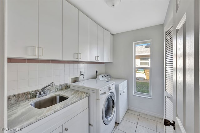 laundry area featuring light tile patterned floors, washing machine and dryer, a sink, baseboards, and cabinet space