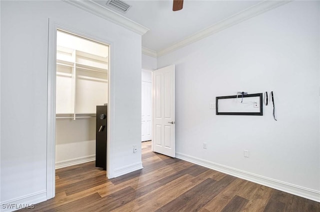 unfurnished bedroom with dark wood-type flooring, ceiling fan, ornamental molding, a walk in closet, and a closet