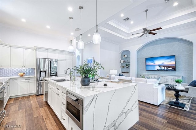 kitchen featuring appliances with stainless steel finishes, a kitchen island with sink, hanging light fixtures, white cabinetry, and light stone countertops