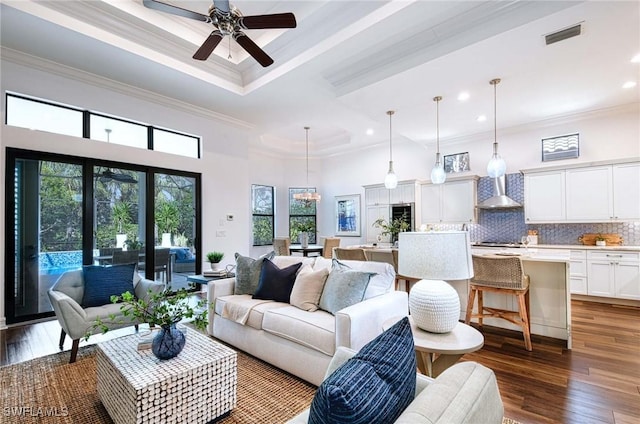 living room with a towering ceiling, ceiling fan with notable chandelier, dark hardwood / wood-style flooring, a tray ceiling, and crown molding