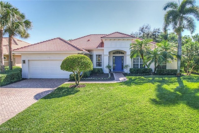 mediterranean / spanish-style home featuring a front lawn, a tiled roof, stucco siding, decorative driveway, and an attached garage