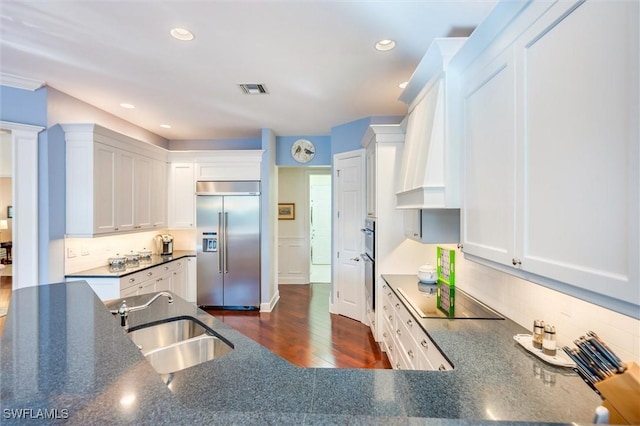 kitchen featuring a sink, decorative backsplash, black electric cooktop, stainless steel built in refrigerator, and white cabinets