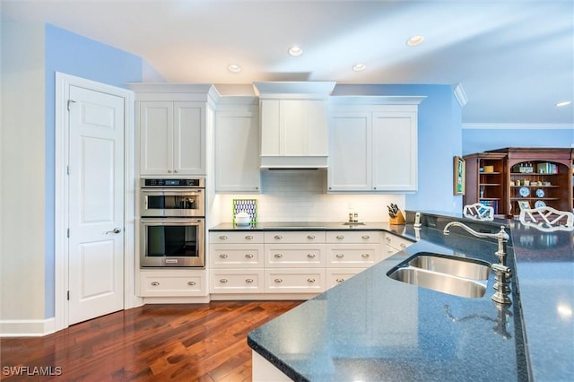 kitchen with dark wood-style floors, stainless steel double oven, ornamental molding, a sink, and white cabinets