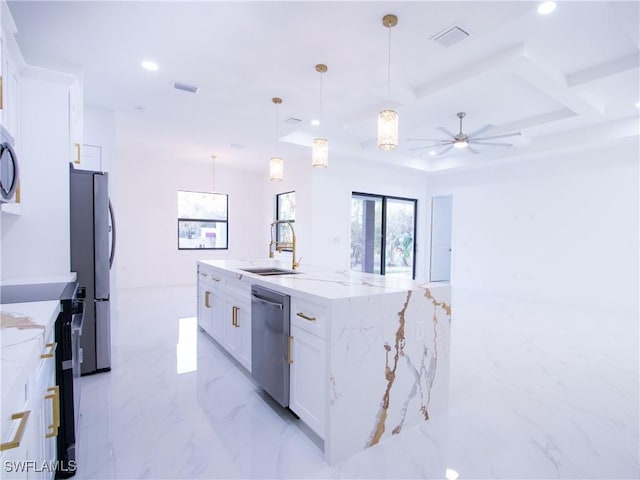 kitchen featuring pendant lighting, appliances with stainless steel finishes, light stone countertops, an island with sink, and white cabinets