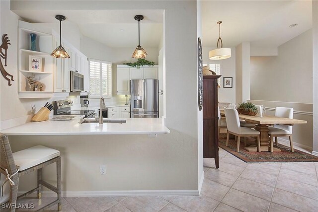 kitchen featuring stainless steel appliances, a sink, white cabinets, a peninsula, and light countertops