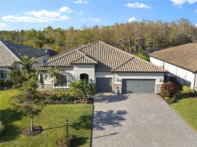 view of front of home with decorative driveway, a tile roof, stucco siding, a garage, and stone siding