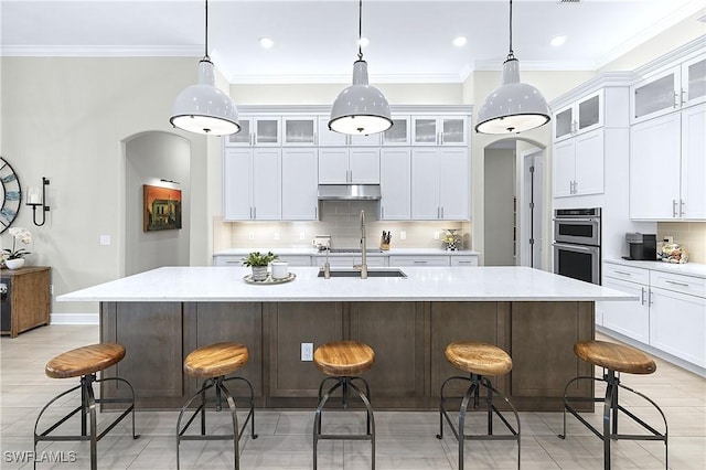 kitchen with white cabinetry, hanging light fixtures, a kitchen breakfast bar, and an island with sink