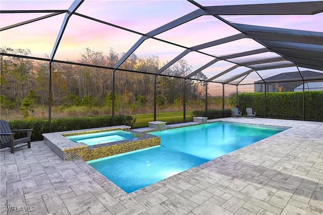 pool at dusk with an in ground hot tub, a patio area, and glass enclosure