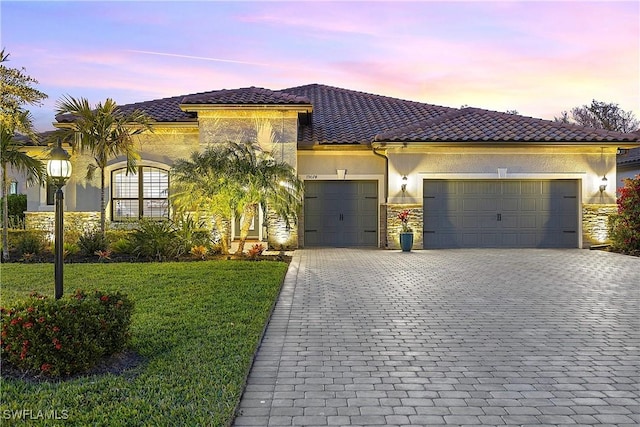 mediterranean / spanish home featuring an attached garage, stone siding, decorative driveway, stucco siding, and a front lawn