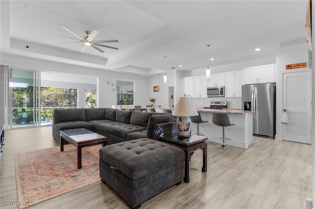 living room featuring a tray ceiling, light hardwood / wood-style floors, and ceiling fan