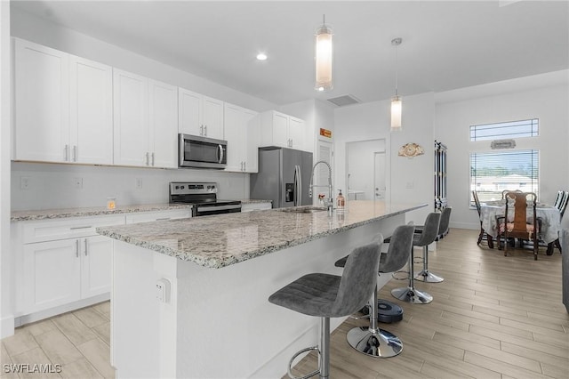 kitchen with a kitchen island with sink, pendant lighting, stainless steel appliances, and white cabinetry