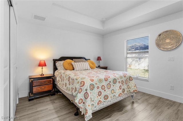 bedroom featuring wood-type flooring, a raised ceiling, and a closet