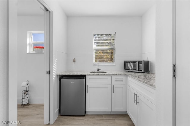 kitchen featuring white cabinetry, sink, light stone counters, and stainless steel refrigerator