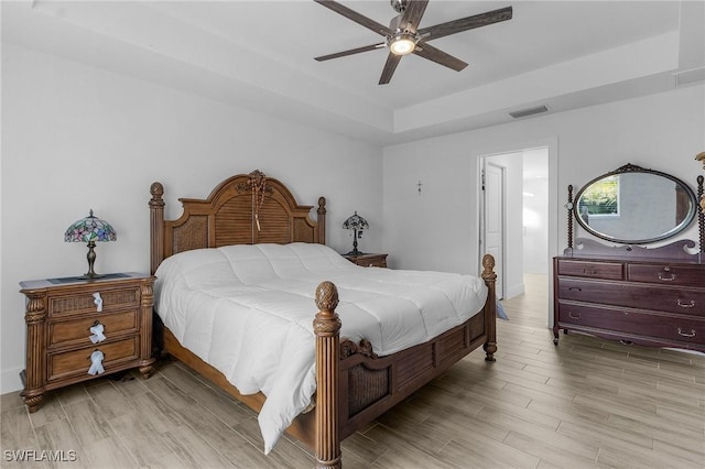 bedroom with a tray ceiling, ceiling fan, and light wood-type flooring