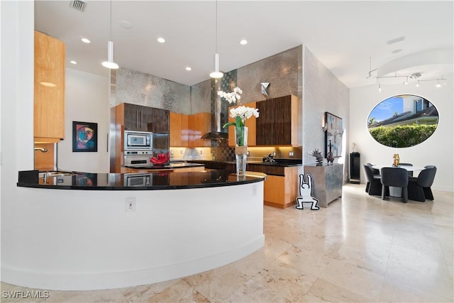 kitchen featuring hanging light fixtures, wall chimney range hood, stainless steel appliances, and a high ceiling