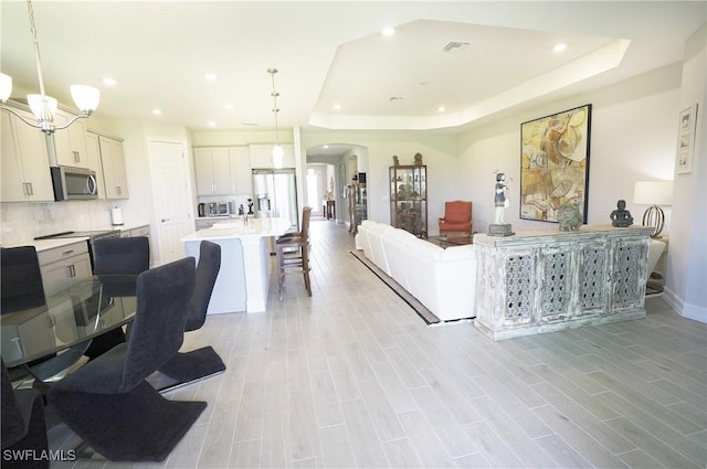 living room with a notable chandelier, light hardwood / wood-style floors, and a tray ceiling