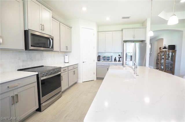 kitchen with tasteful backsplash, decorative light fixtures, stainless steel appliances, and light wood-type flooring