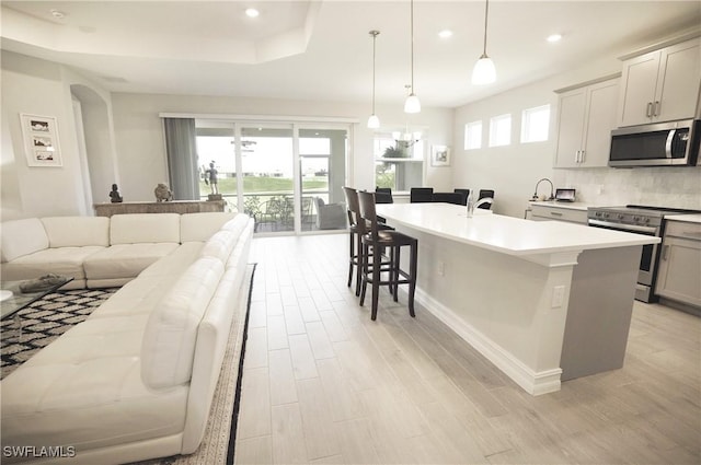 kitchen featuring a kitchen bar, decorative light fixtures, appliances with stainless steel finishes, a wealth of natural light, and a kitchen island with sink