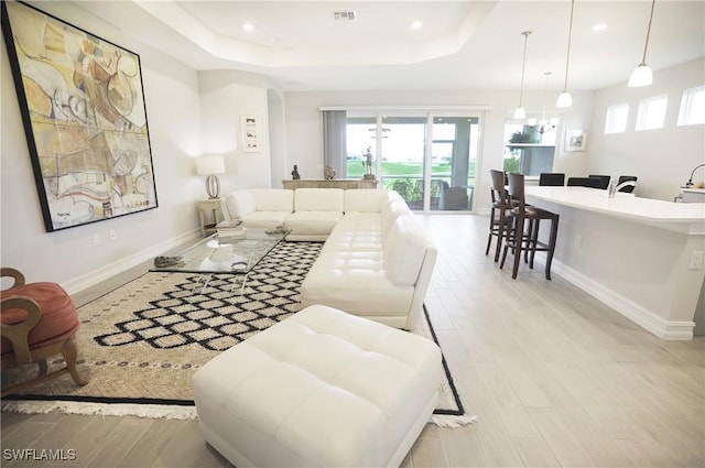 living room featuring a raised ceiling, light hardwood / wood-style flooring, and a wealth of natural light