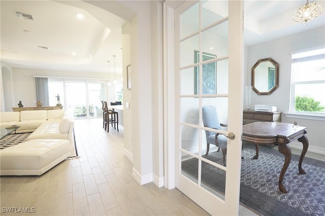 interior space with french doors, a wealth of natural light, light hardwood / wood-style floors, and a tray ceiling